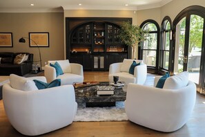 Una sala de estar moderna con sofás blancos, una mesa de centro de mármol y un mueble de madera oscura con puertas de vidrio.