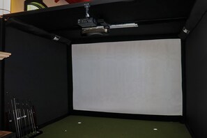 Una habitació amb un projector fixat al sostre, una pantalla en blanc i una catifa verda.