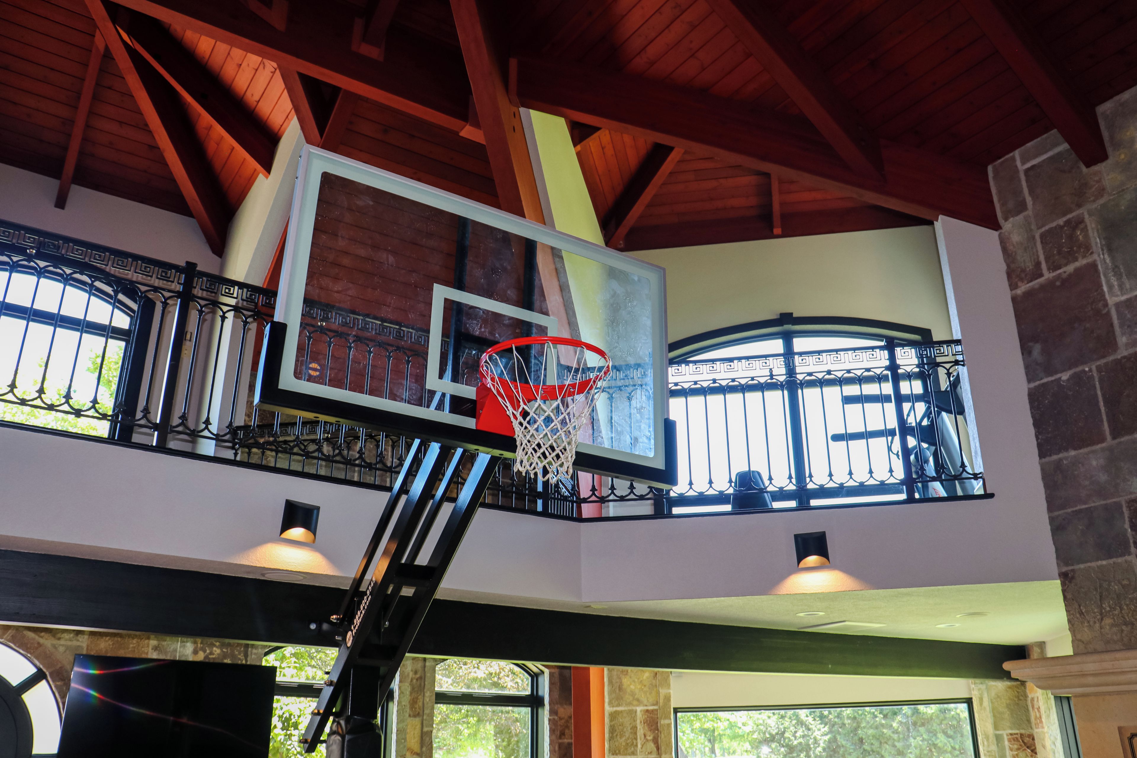 Un panier de basket avec un panneau et un filet, un escalier menant à un niveau supérieur, et une fenêtre ornée d’une grille décorative.