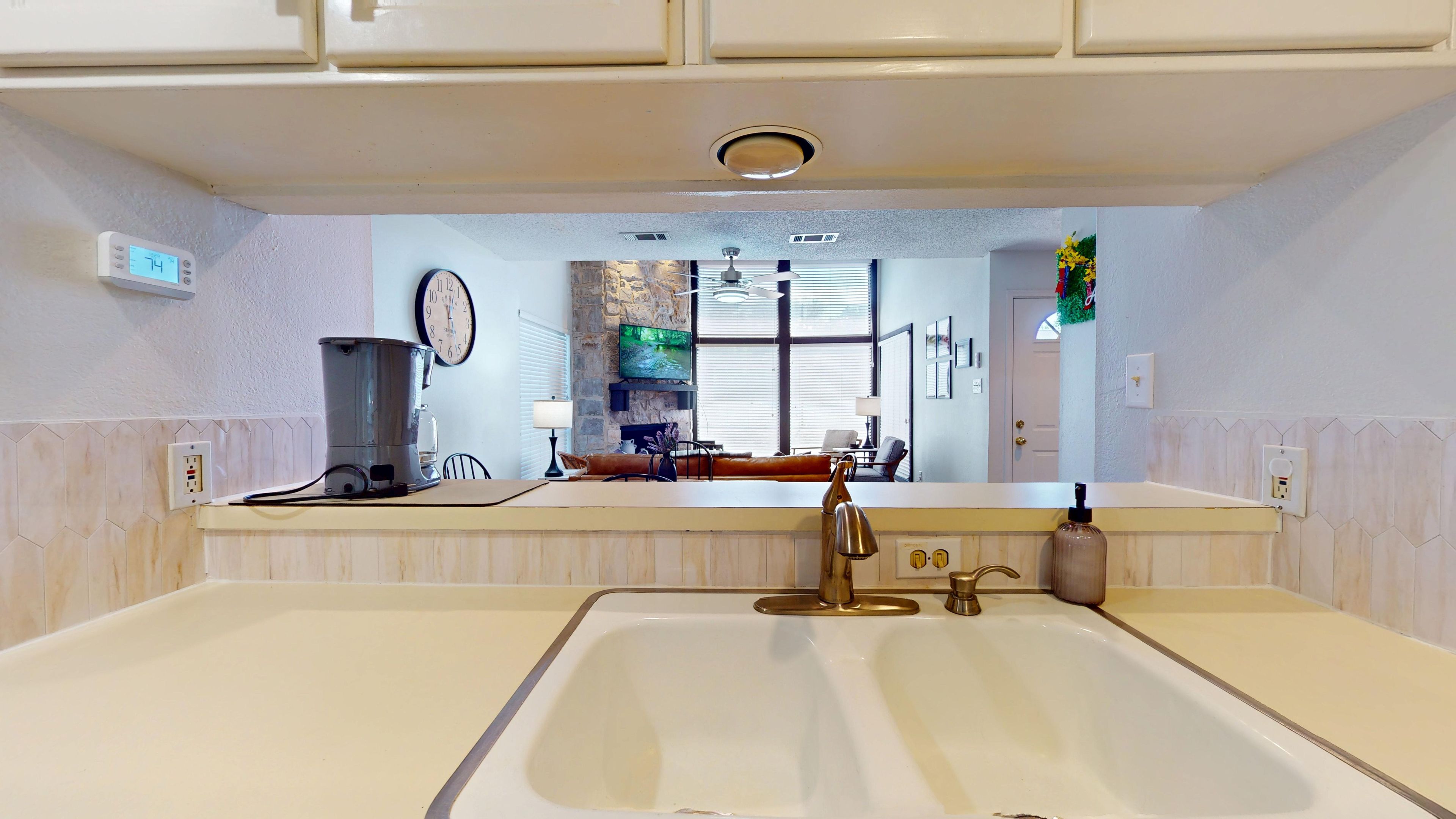 A kitchen with a large sink, a coffee maker, a clock, and a television.