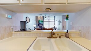A kitchen with a large sink, a coffee maker, a clock, and a television. - River City Resorts: Among the Oaks T-Bar-M 112: Spacious Hill Country Condo. (New Braunfels)