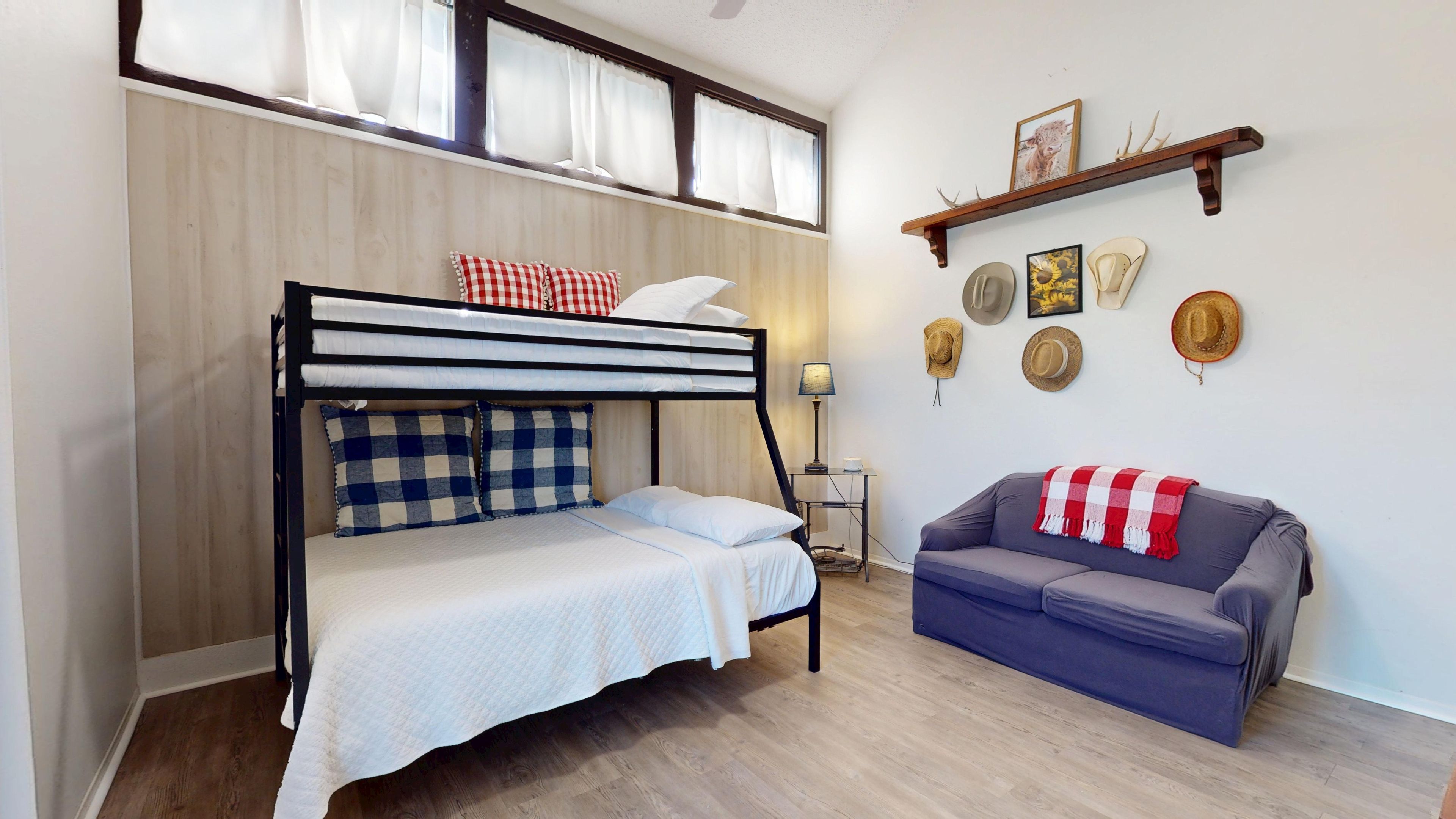 Ein Zimmer mit einem Etagenbett, einer Schlafcouch und einem an der Wand befestigten Regal mit Hüten.