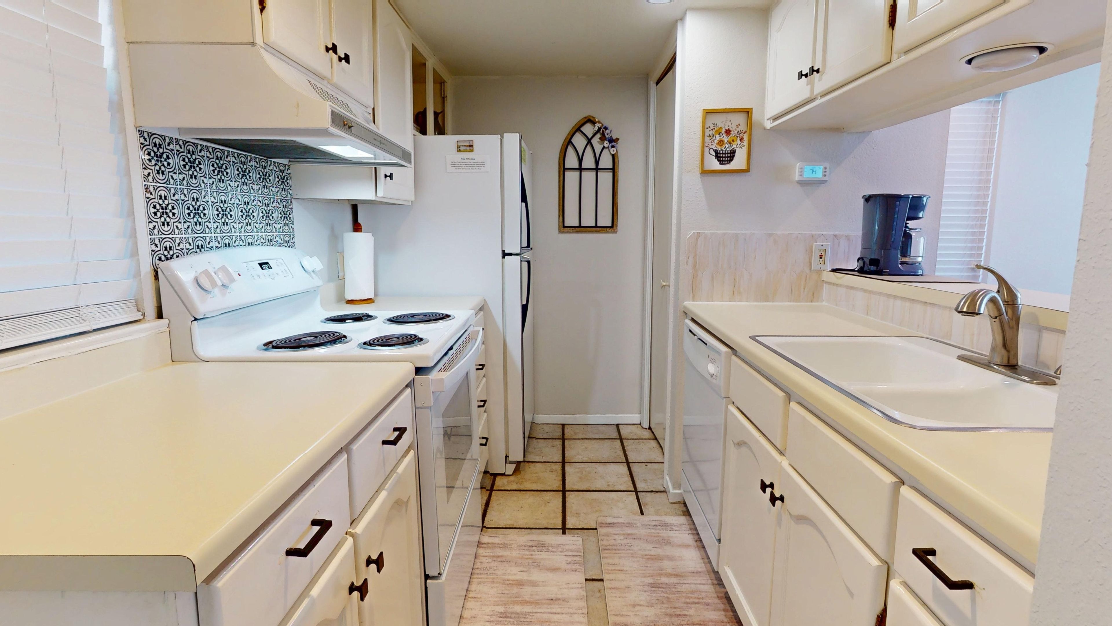 Una cocina estrecha con armarios blancos, una estufa, un refrigerador y un lavamanos.