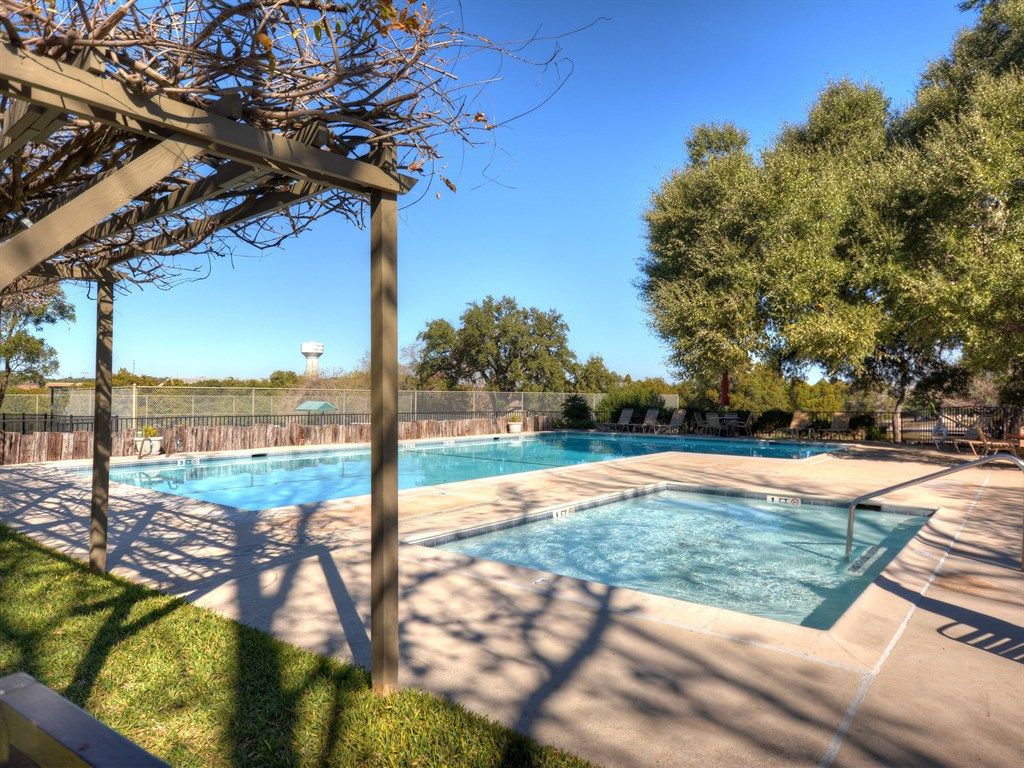A rectangular swimming pool with a pergola overhead, surrounded by a fence and trees.