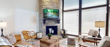 A cozy living room with a stone fireplace, comfortable seating, and large windows.