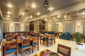 Ein Restaurant mit mehreren Tischen, Stühlen, einem grünen Sofa und einem Blumentopf.