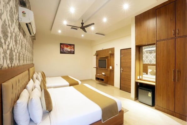 A hotel room with two beds, a ceiling fan, a TV, and a minibar. - Signature Prime By Indicott (Jaipur)