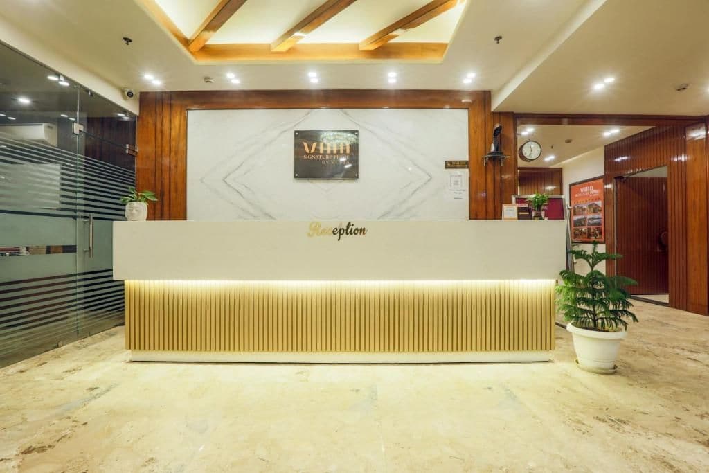 Un comptoir d’accueil avec un plateau en marbre, un panneau décoratif en bois et une enseigne indiquant « VHH Signature Place ».