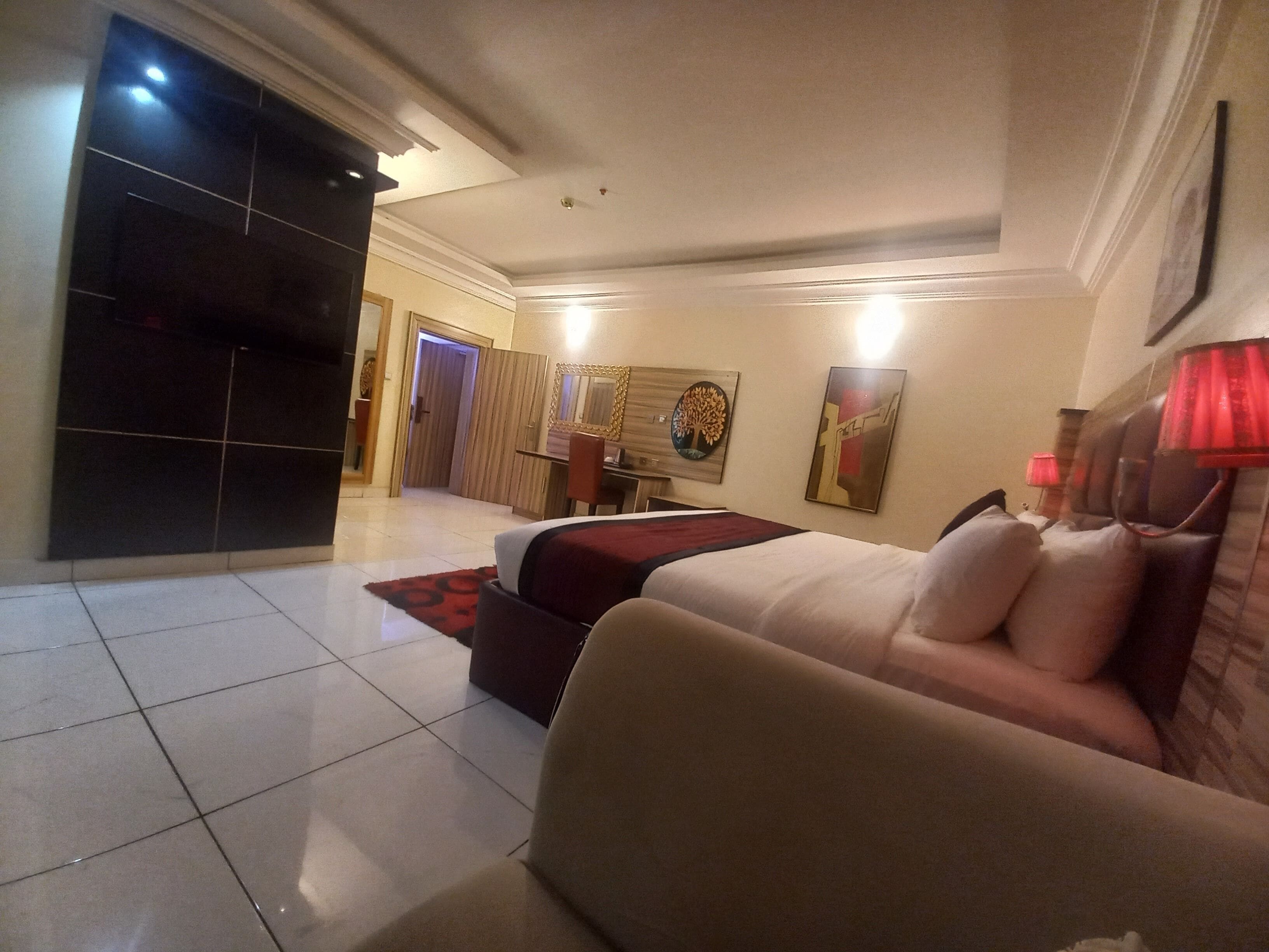 A hotel room with a bed, a desk, and a chair. There is a door leading to another room.