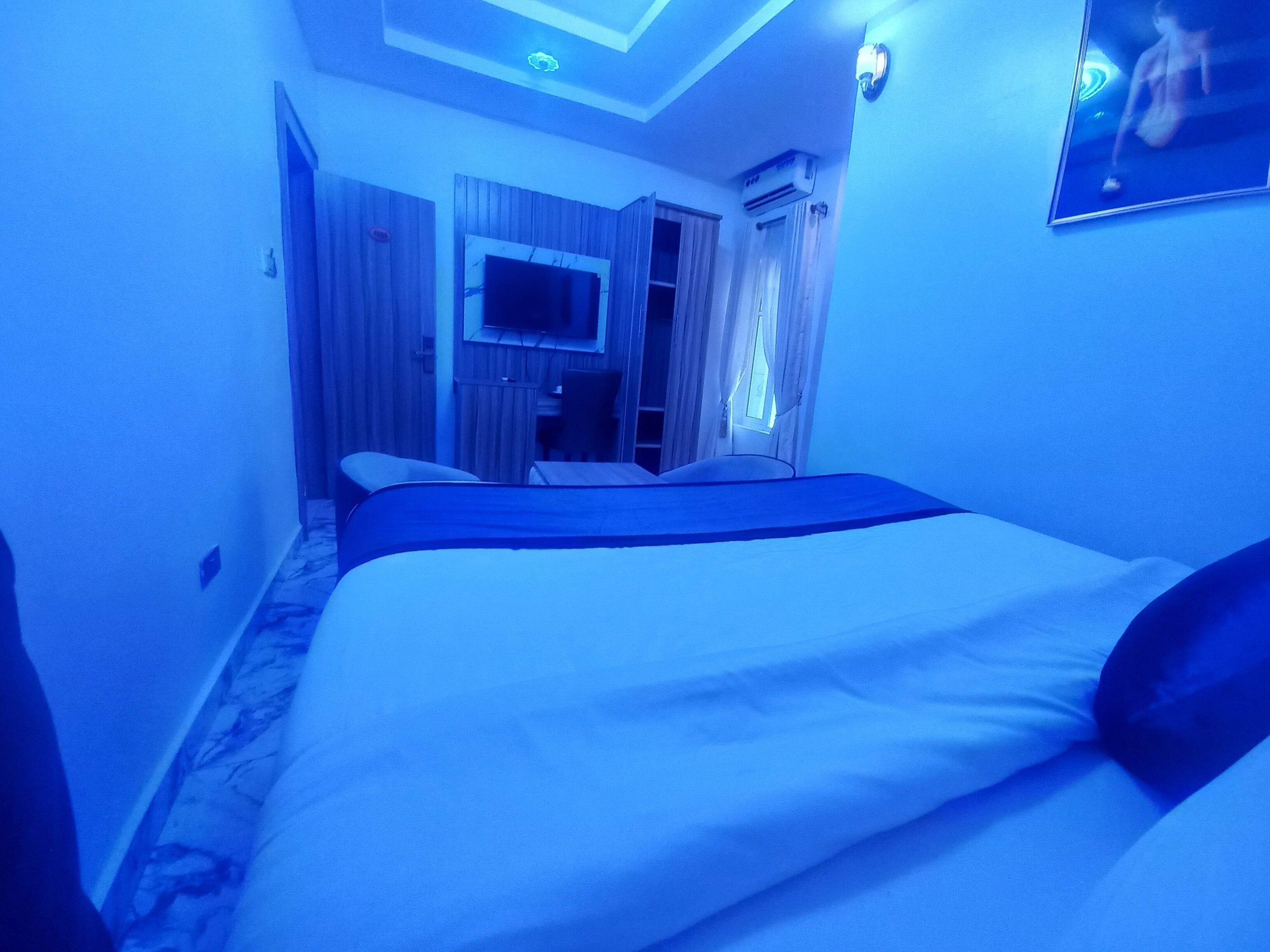 Una habitación de hotel con una cama, un televisor montado en la pared y una ventana con cortinas.