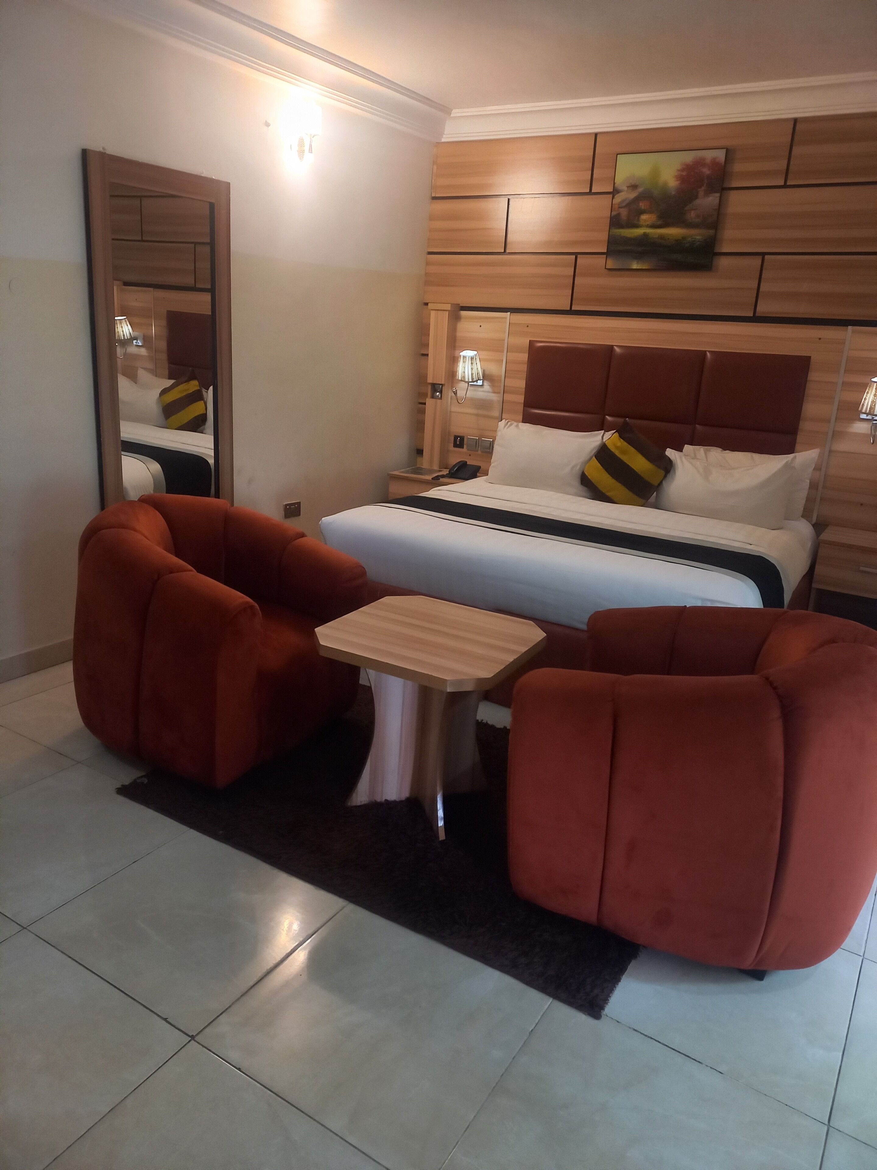 Habitación de hotel con cama, dos sillones, una mesita, un espejo y un cuadro en la pared.