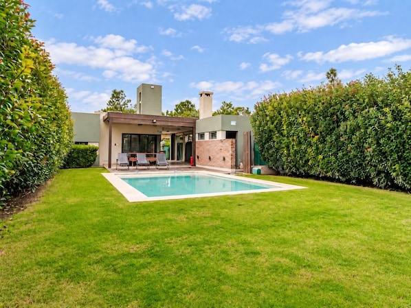 A modern house with a swimming pool, a patio with chairs, and a well-maintained lawn.