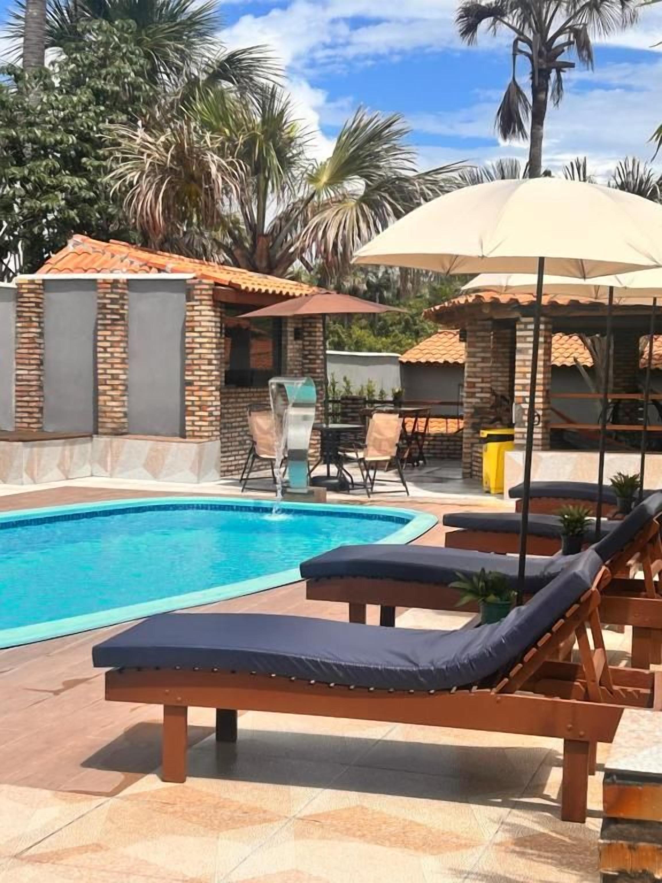 A pool area with lounge chairs and umbrellas, surrounded by brick walls and palm trees.