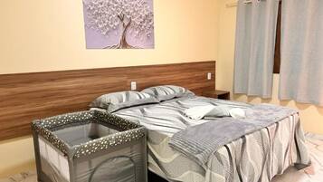 Un dormitorio con cama, cabecera, una obra de arte en la pared, una ventana con cortinas y un área pequeña y cerrada con un forro estampado.