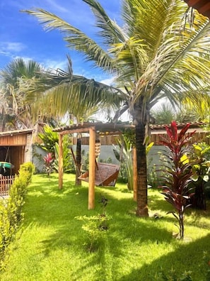 Un jardín tropical con palmeras, una hamaca y una pérgola de madera.
