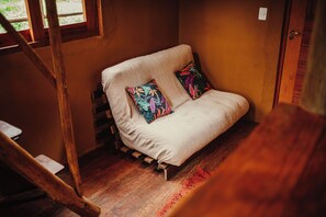Ein gemütliches Zimmer mit Holzboden, einer Couch mit gemusterten Kissen und einem Fenster mit Blick.