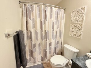 Et badeværelse med bruseforhæng, toilet og dekorativ vægpanel.