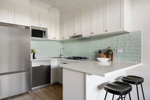 A modern kitchen with white cabinetry, a stainless steel refrigerator, a gas stove, and a white countertop. - Urban Rest Bondi Park (Bondi)