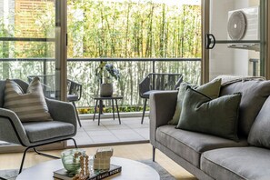 A modern living room with a grey sofa, armchairs, and a coffee table. There is a balcony with a view of bamboo trees. - Urban Rest Bondi Park (Bondi)
