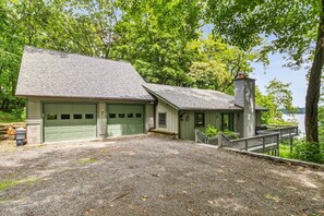 A two-story house with a garage, a chimney, and a deck overlooking a body of water. - Gorgeous 3BR Lakeview Adirondacks Dog Friendly (Hague)