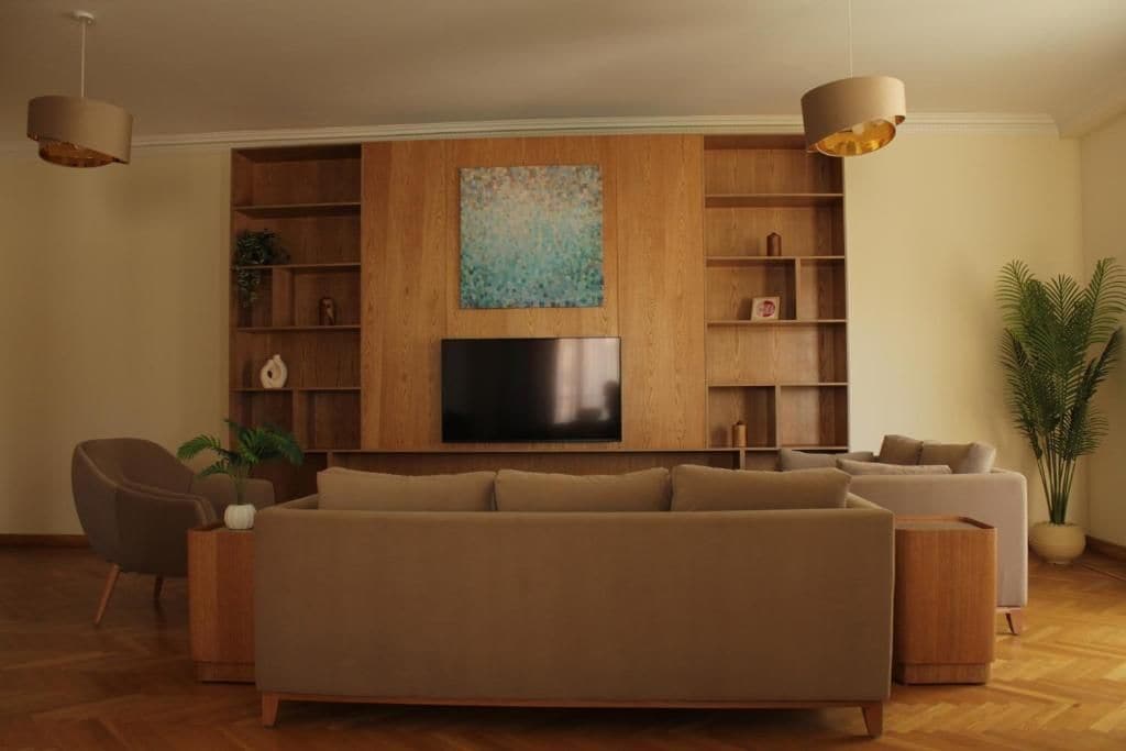 Ein modernes Wohnzimmer mit einem großen Flachbildfernseher, Holzregalen und zwei Pendelleuchten.