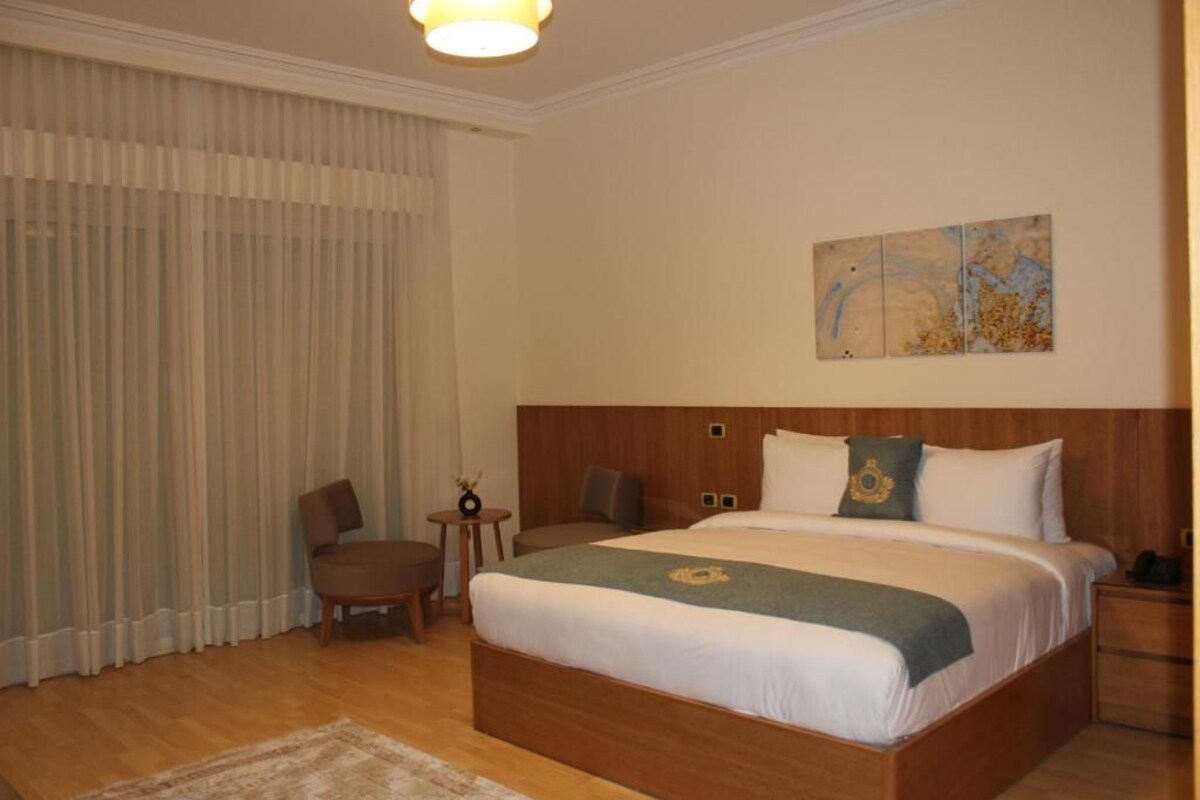 A hotel room with a large bed, a wooden headboard, a small table, a chair, and a painting on the wall.