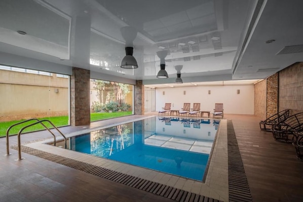 A swimming pool with a view of a garden and a building in the background. - The 88th Signature by Maran Hospitality (New Cairo)