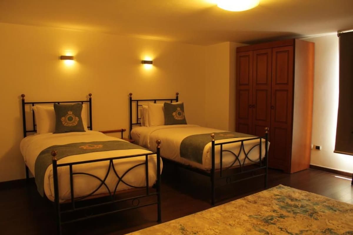 A room with two beds, each with a headboard and pillows, a wooden wardrobe, and a carpet.