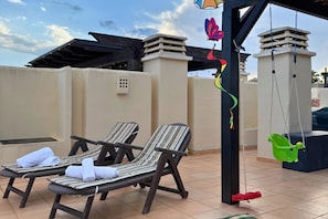 Two sun loungers with towels, a hanging swing, and a view of a building with a flat roof. - Casa Del Sol by Rental Hero (Pozo Aledo)