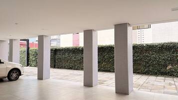 A spacious indoor area with tiled flooring, large pillars, and a white car parked in the foreground.