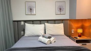 Habitación de hotel con cama, almohadas, mesita de noche con lámpara y dos cuadros en la pared.