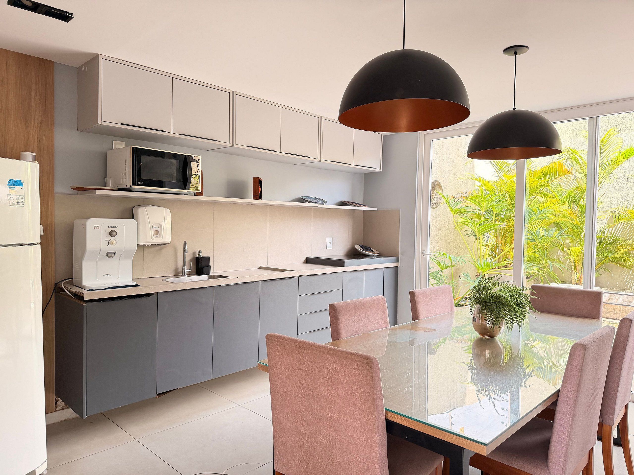 Una cocina moderna con armarios grises, un microondas, una cafetera y un comedor con mesa de vidrio y sillas rosadas.