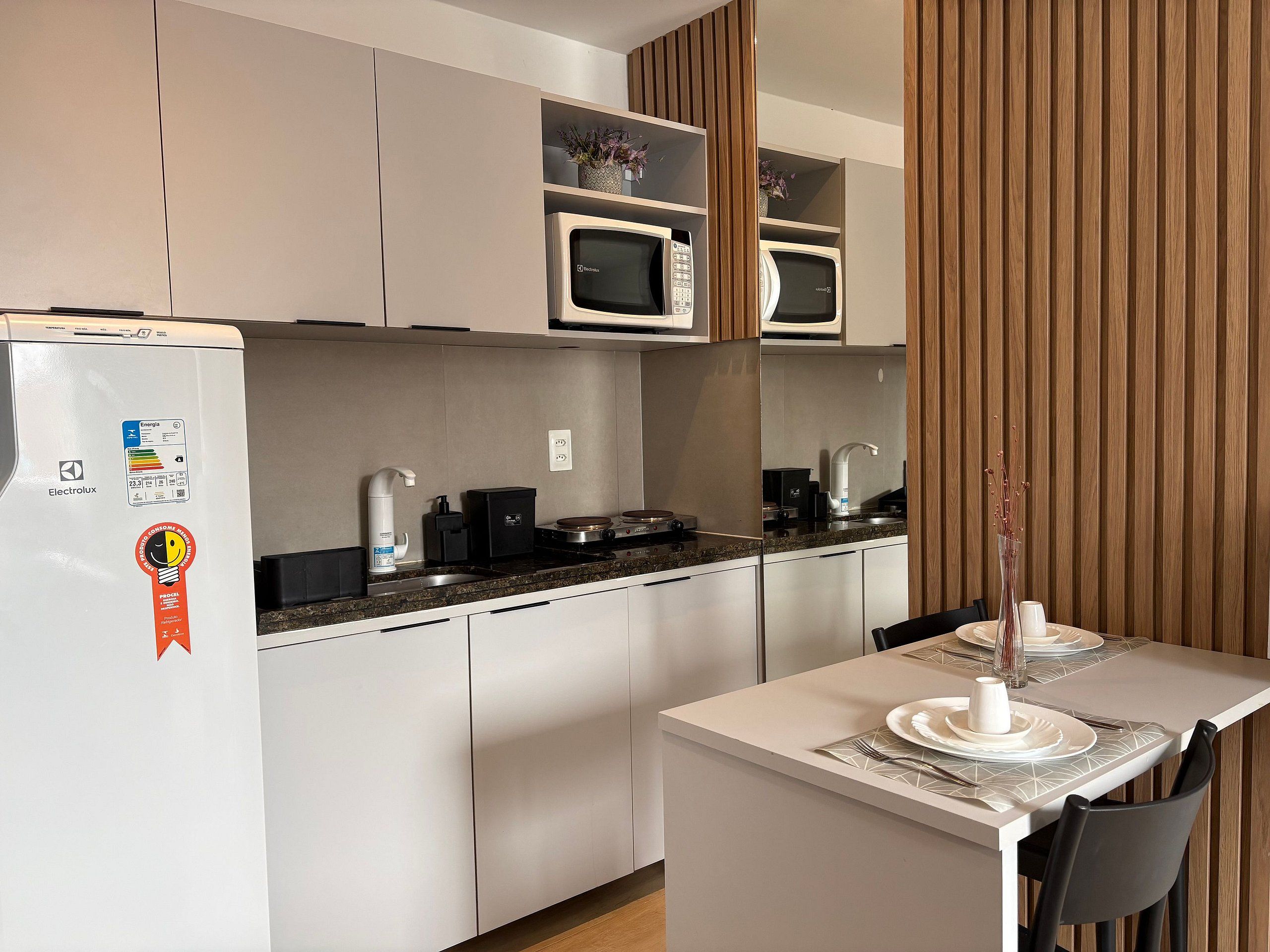 Cocina compacta con refrigerador, microondas y estufa, una mesa de comedor con sillas, y un revestimiento de pared de madera.