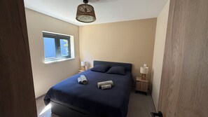 A bedroom with a bed, two bedside lamps, a window, and a ceiling light fixture.