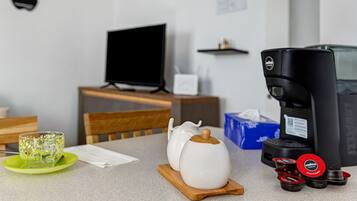 Un angolo cottura con una macchina da caffè, un bollitore, una tazza di vetro e un televisore su un tavolo in legno.
