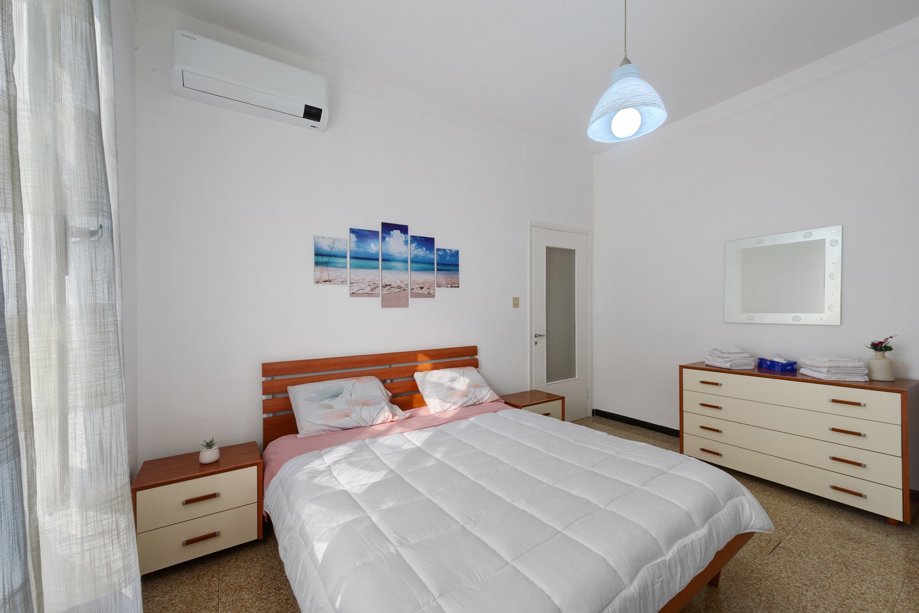 A bedroom with a bed, bedside tables, a dresser, a mirror, and a wall-mounted air conditioner.