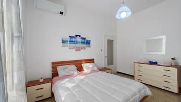 A bedroom with a bed, bedside tables, a dresser, a mirror, and a wall-mounted air conditioner.