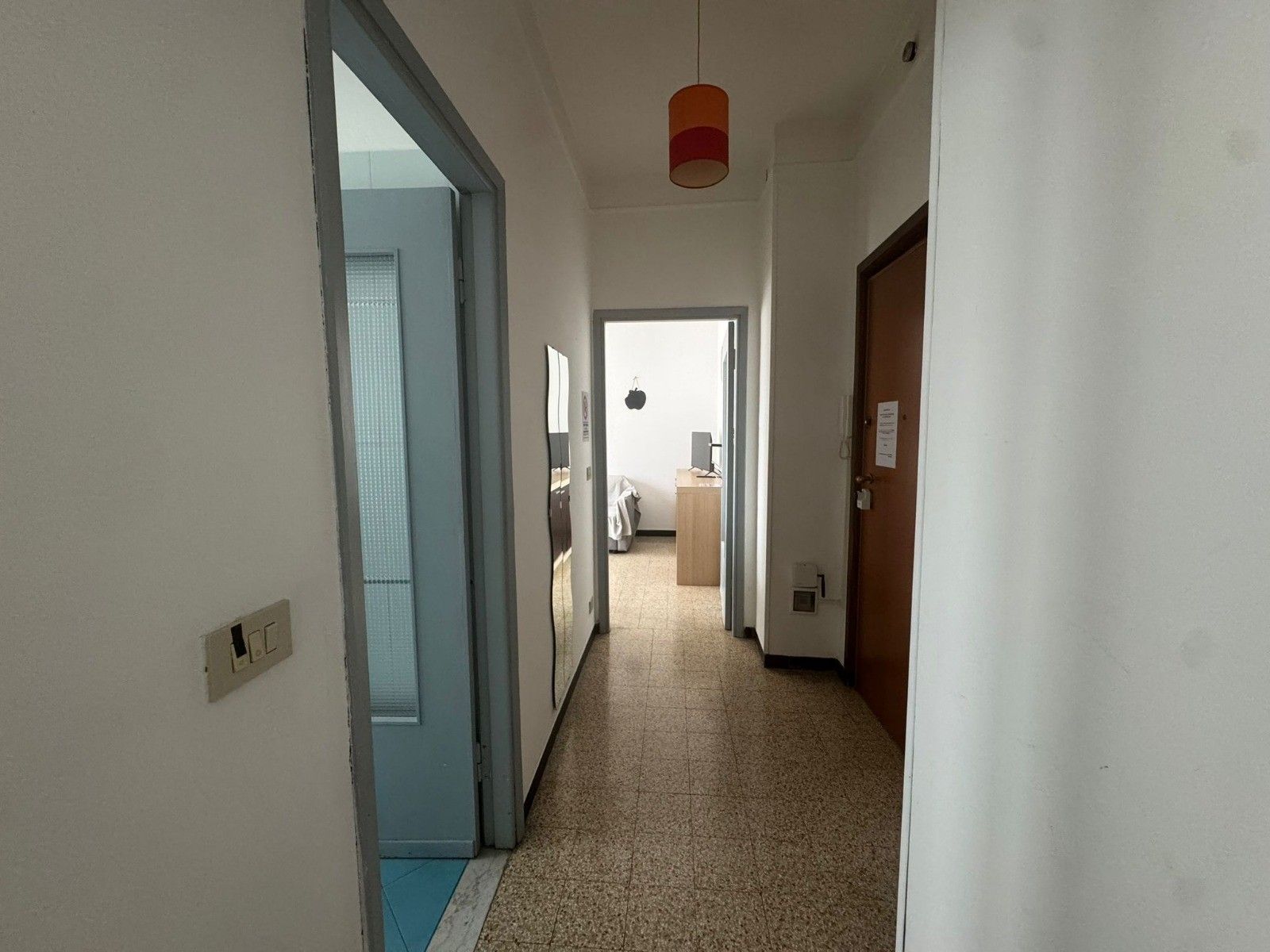 A hallway with a door on the right, a light fixture above, and a window on the left.