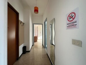 Ein Flur mit einer Tür links, einer Leuchte darüber und einem Rauchverbot-Schild an der Wand.