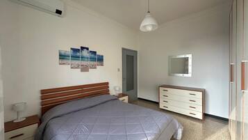 Ein Schlafzimmer mit Bett, Nachttisch, Lampe, Kommode, Spiegel und Wandbildern.