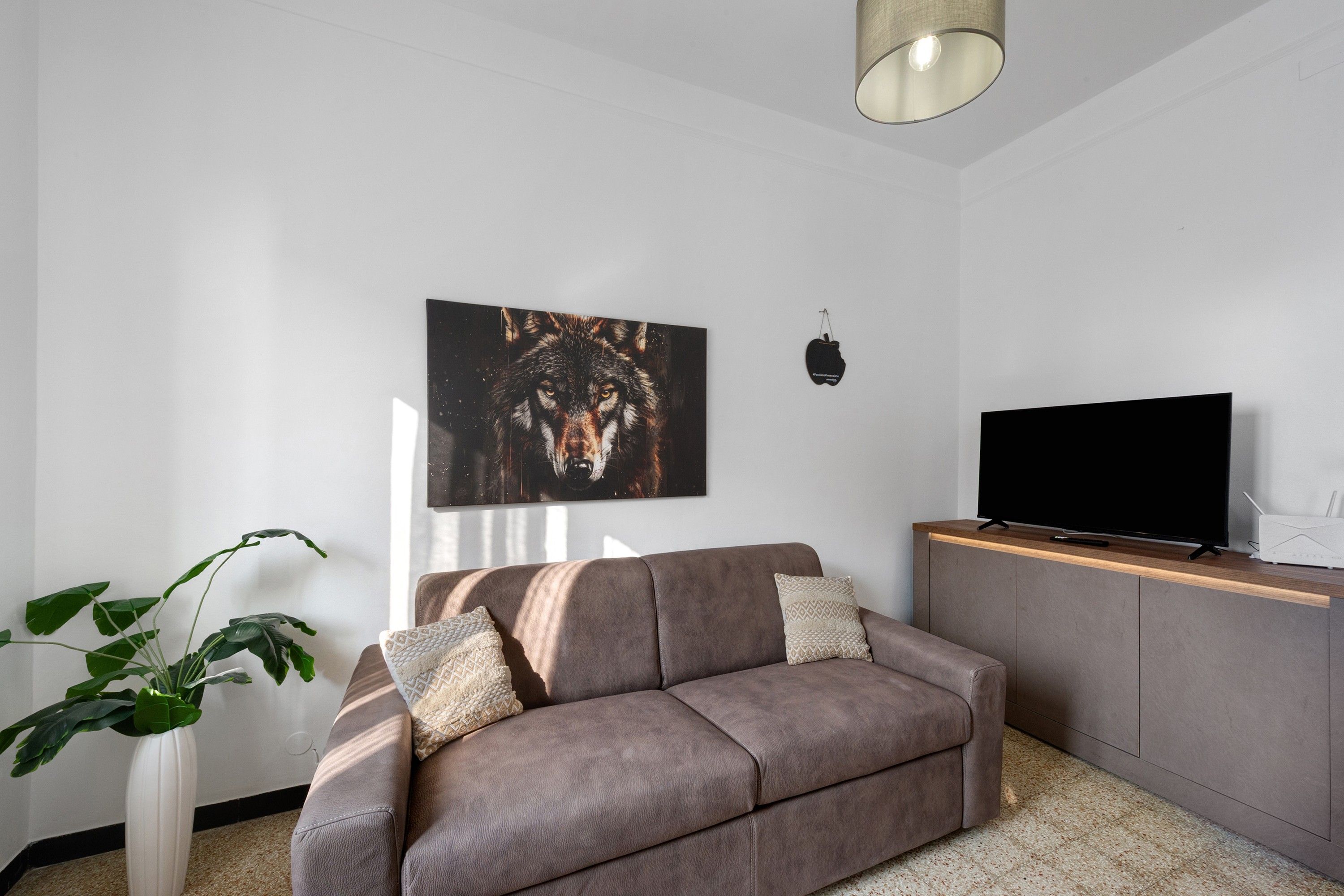 Un soggiorno moderno con un divano, una TV a schermo piatto, una pianta e un’opera d’arte appesa al muro.