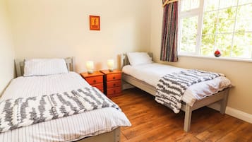 A bedroom with two single beds, wooden nightstands with lamps, a window with curtains, and a wall-mounted picture.
