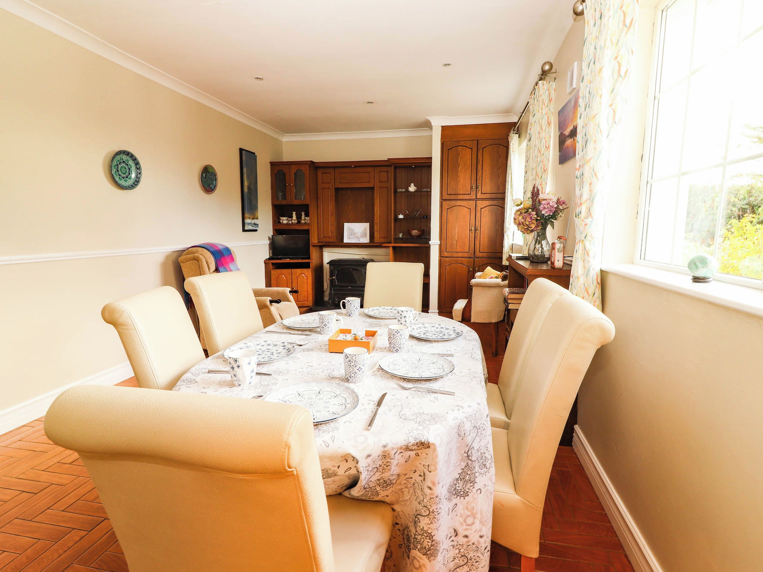 A dining area with a table set for four, surrounded by chairs, with a kitchen in the background.