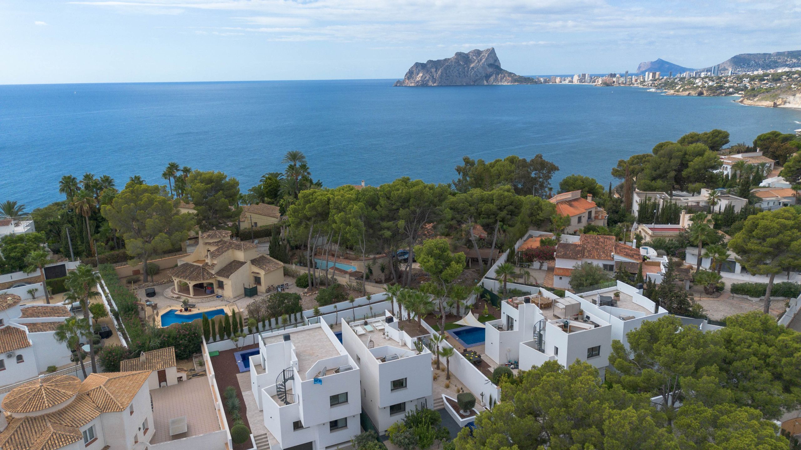 Un quartier résidentiel en bord de mer, avec des maisons modernes, une piscine et une vue sur la mer et une montagne lointaine.
