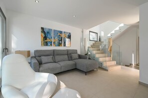 A modern living room with a grey sectional sofa, a white armchair, and abstract wall art. - Villa Cap Blanc, Moraira (Moraira)