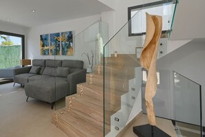A modern living room with a grey sofa, abstract paintings, and a staircase with glass railings. - Villa Cap Blanc, Moraira (Moraira)