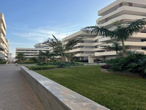 Un edifici residencial de diversos pisos amb balcons, envoltat de gespes ben cuidades i palmeres.