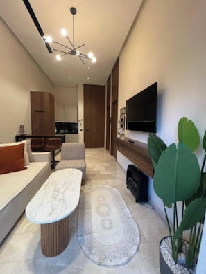 Een moderne woonkamer met een bank, een salontafel, een televisie en een grote plant.