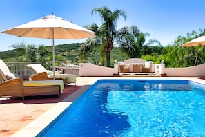 A swimming pool with lounge chairs and umbrellas, surrounded by greenery and hills. - Casa das oliveiras, beautifully situated villa, with mature garden and sw.pool. (Loulé)