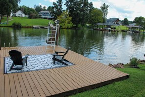 A wooden deck with two chairs and a table, overlooking a calm lake with houses in the background. - Unique 4-bedroom Lake House with Private Dock in Vonore (Vonore)